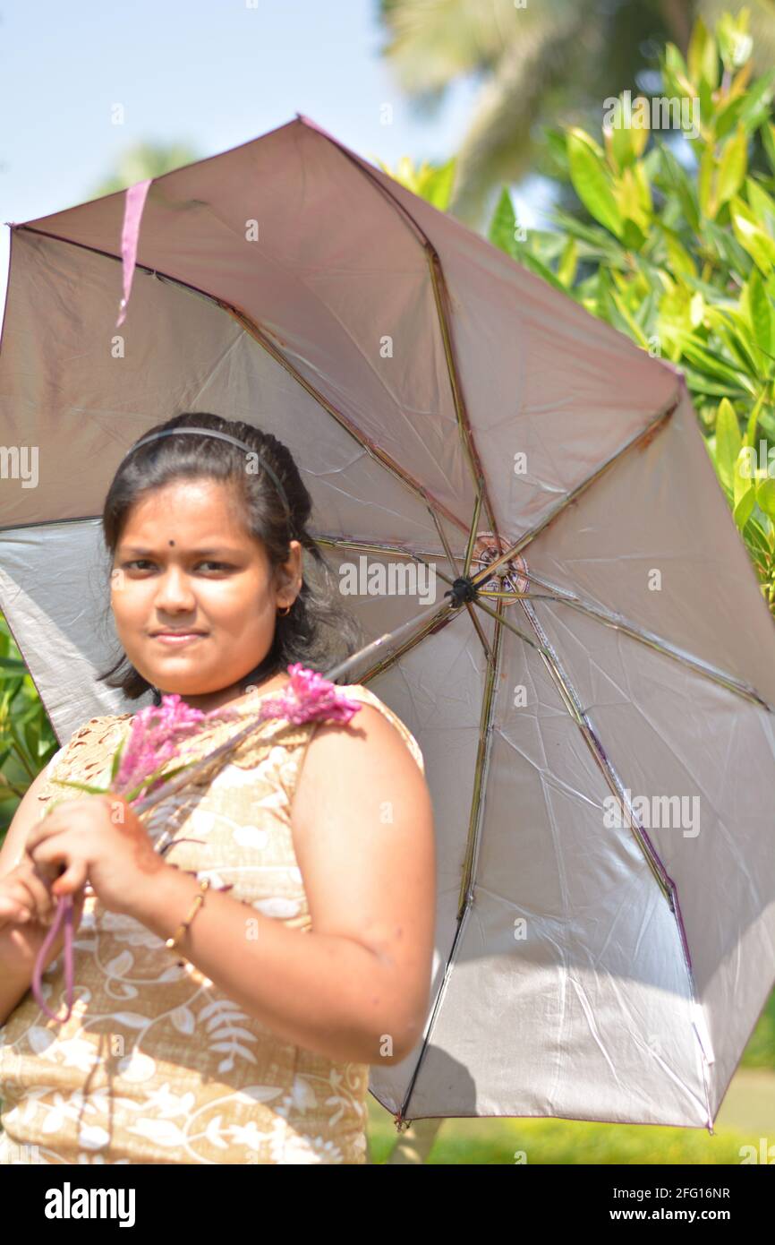 Teenage Indian Bengali girl holding a numbrella on her shoulder posing for photo in a garden, selective focusing Stock Photo
