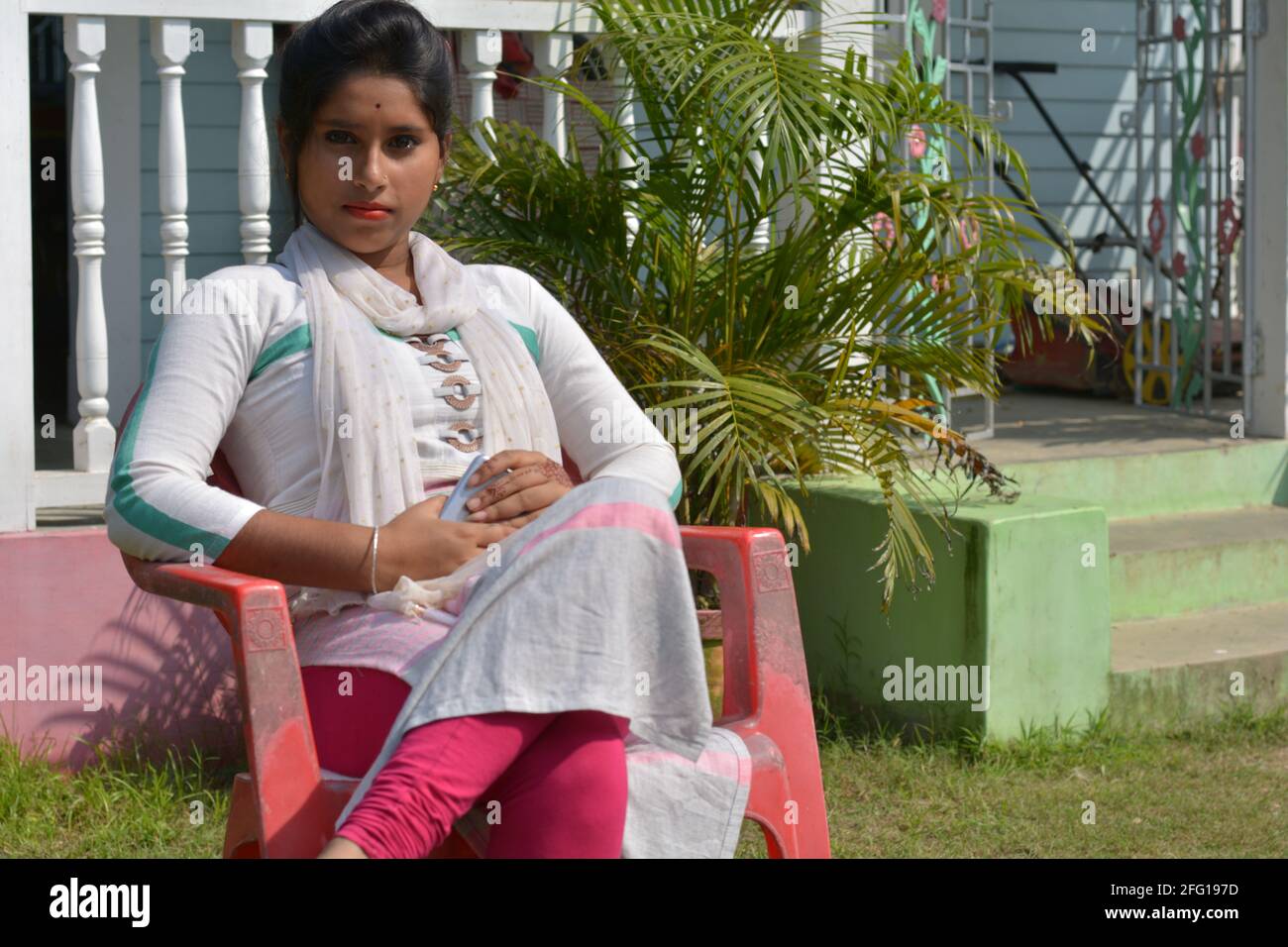 Close up of an Indian Bengali teenage girl wearing traditional  white cotton salwar kameez sitting on a plastic chair, selective focusing Stock Photo