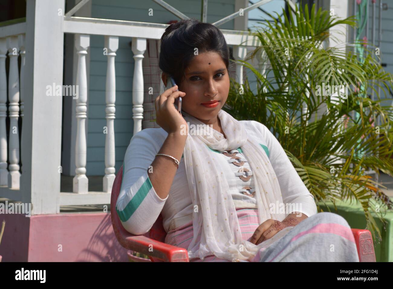 Teenage Indian Bengali girl sitting on a chair talking in mobile phone, selective focusing Stock Photo