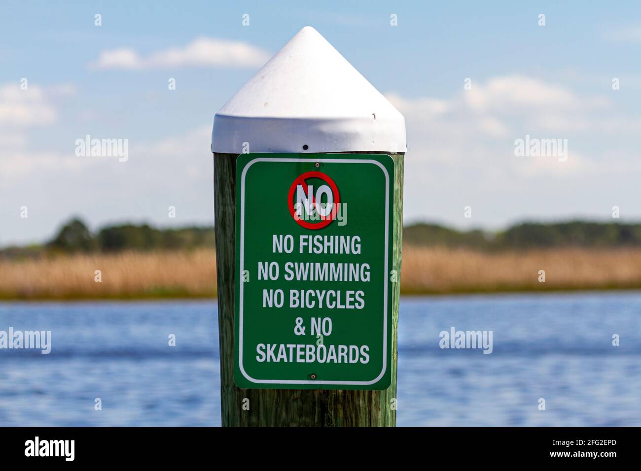 Sign on a dock post by the sea says no swimming, diving, cycling or skateboarding on the pier. Versatile image with health and safety or  restricitive Stock Photo