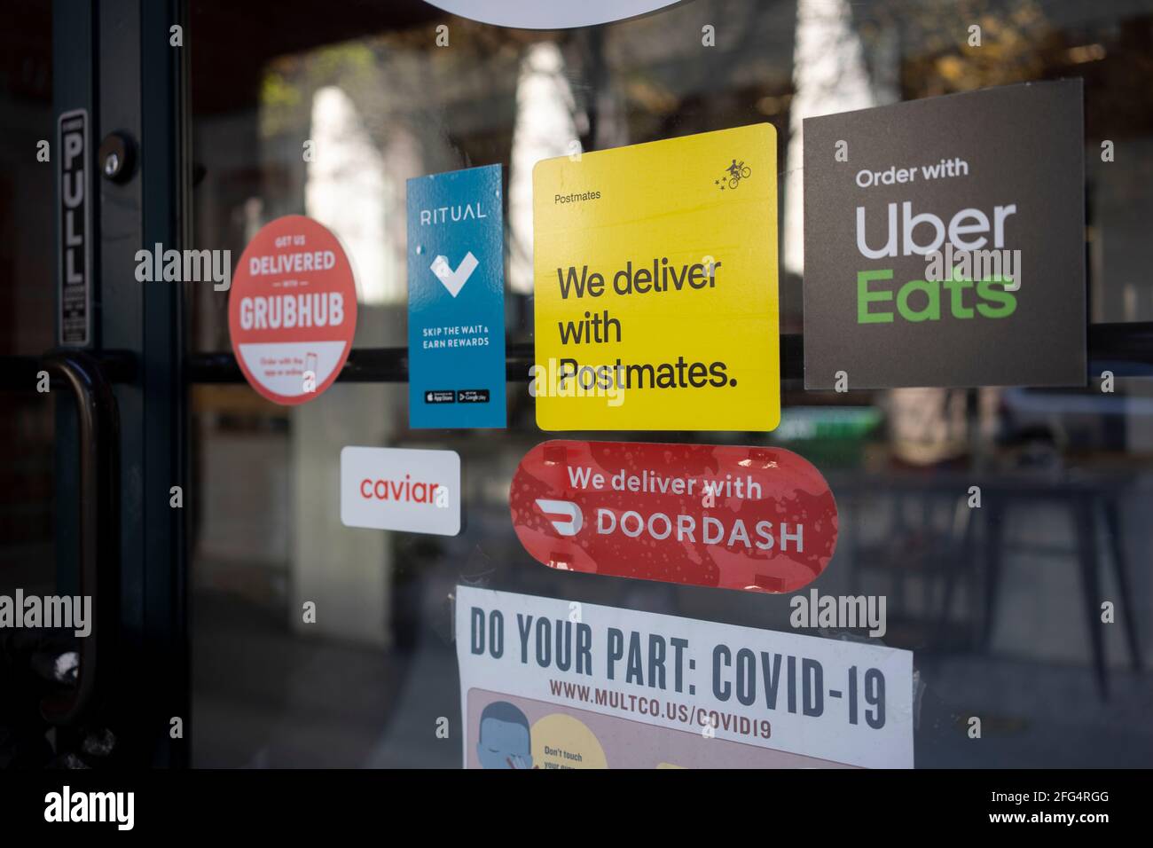 Various food delivery service options - DoorDash, Postmates, Uber Eats, Ritual, Caviar, and Grubhub - are seen advertised at the entrance to a restaurant... Stock Photo