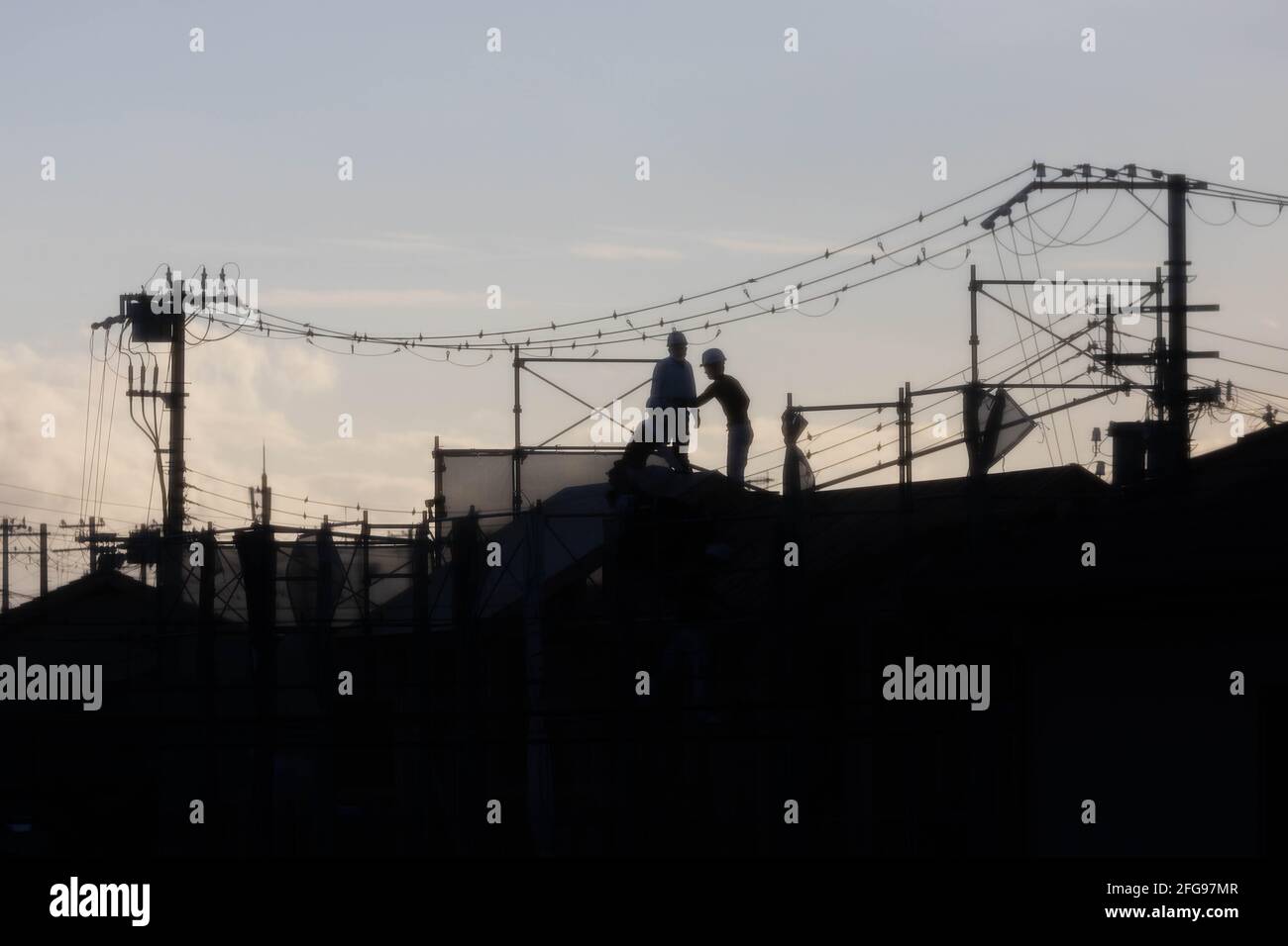Workers on roof under electrical wires at sunset Stock Photo