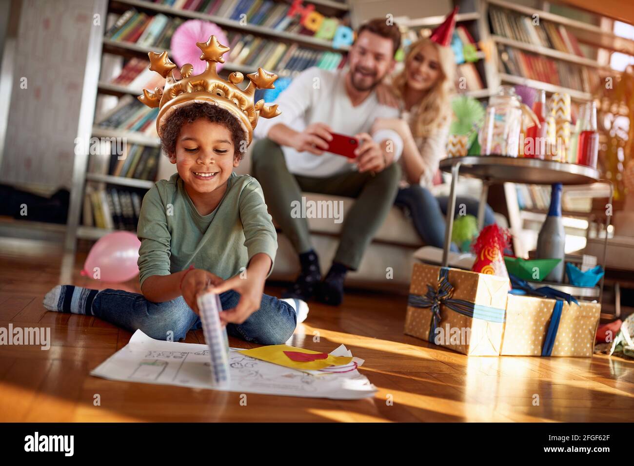 Happy couple taking a photo of their adopted little boy while playing at kids birthday party in a cheerful atmosphere at home. Family, celebration, to Stock Photo