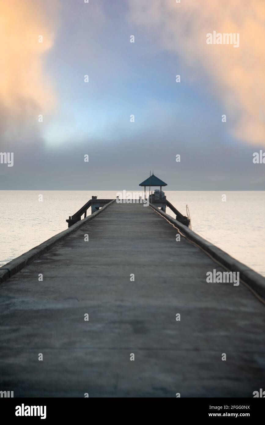 Silhouette of concrete bridge extends into the sea on a cloudy day in ...