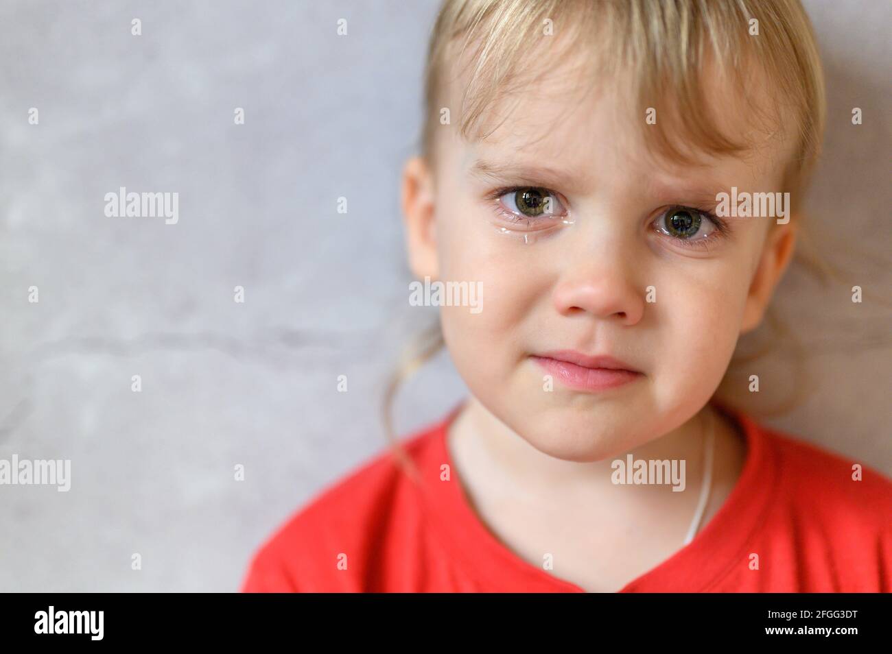 kid crying. the face of a cute little upset four year old baby boy in tears. children's grief. gray concrete wall background. space for text Stock Photo