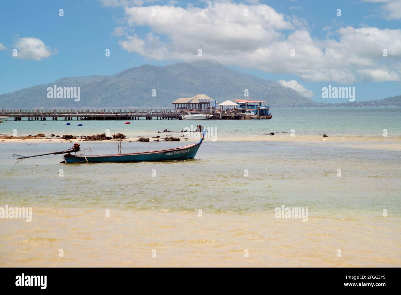 Tropical beach scenery with LongTail boats in the sea, blue sky and white clouds in summer and with a harbor in the background. Stock Photo
