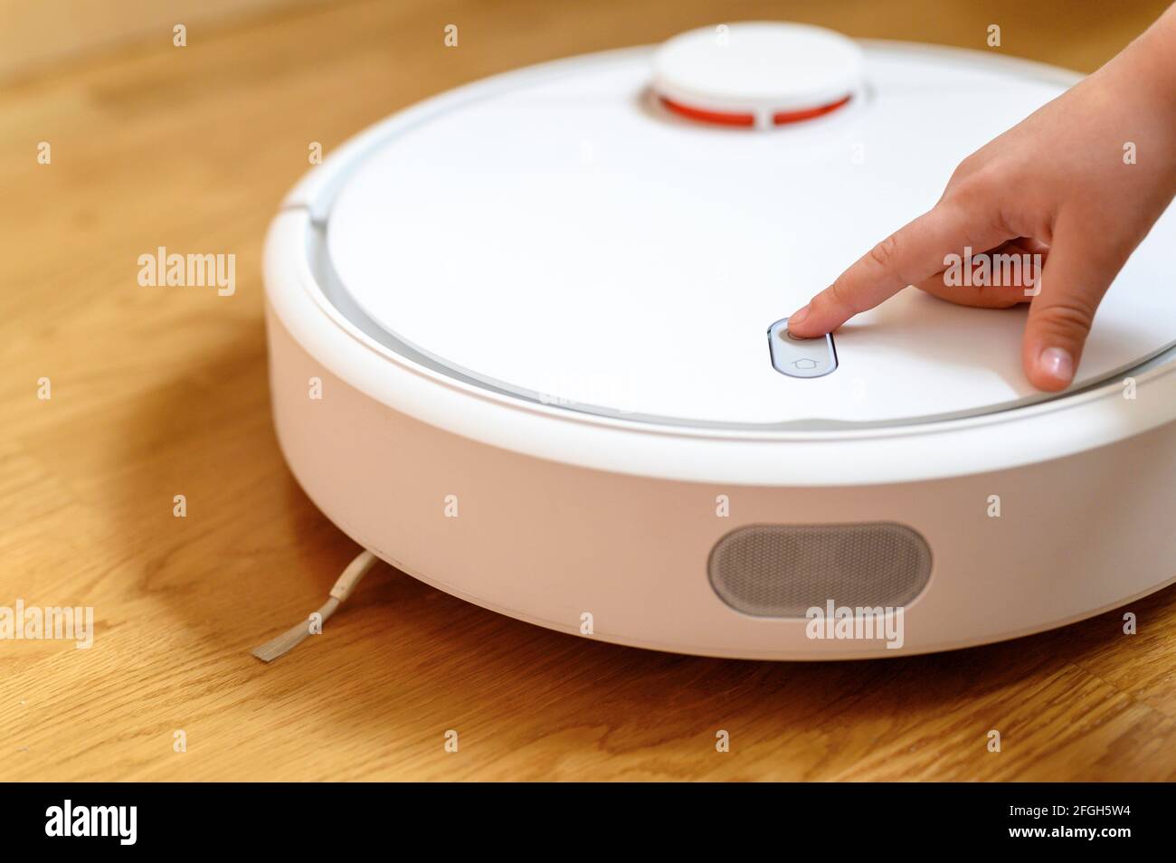 a kids hand presses the button to turn the robot vacuum cleaner on