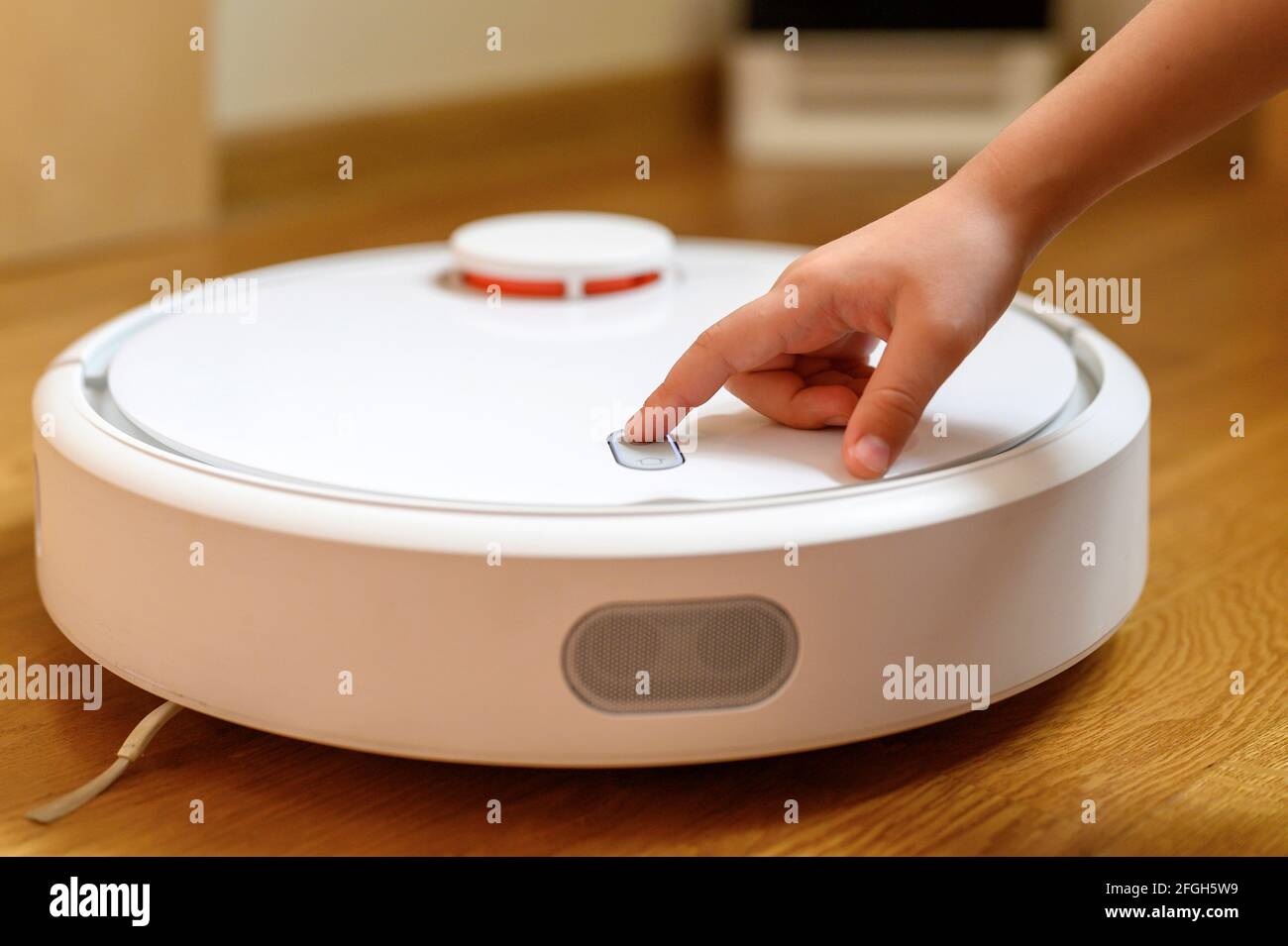 a kids hand presses the button to turn the robot vacuum cleaner on