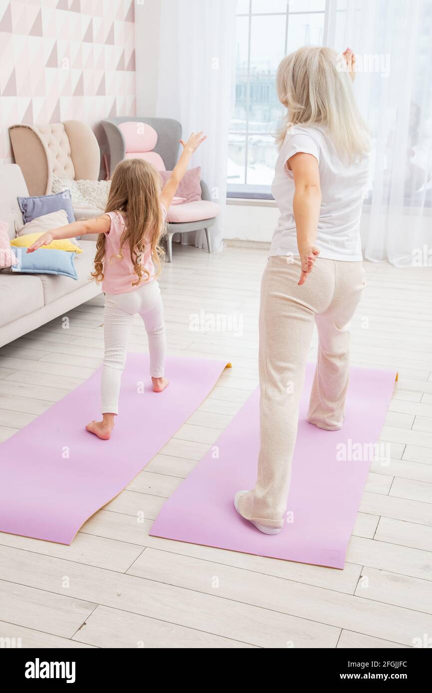 Full length back side view smiling blond mother on yoga mat with