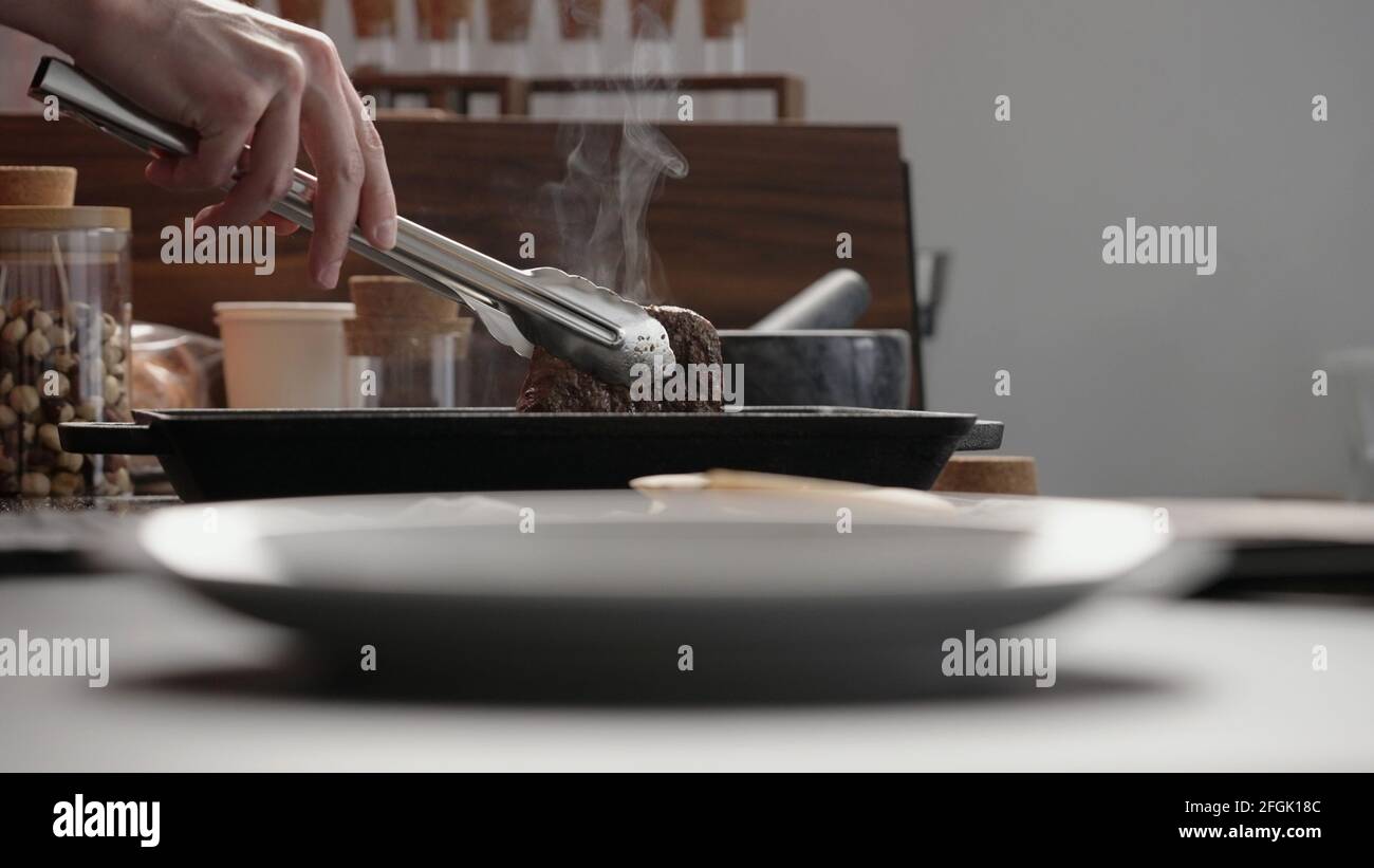 man hand use tongs to pick up beef steak from grill pan, wide photo