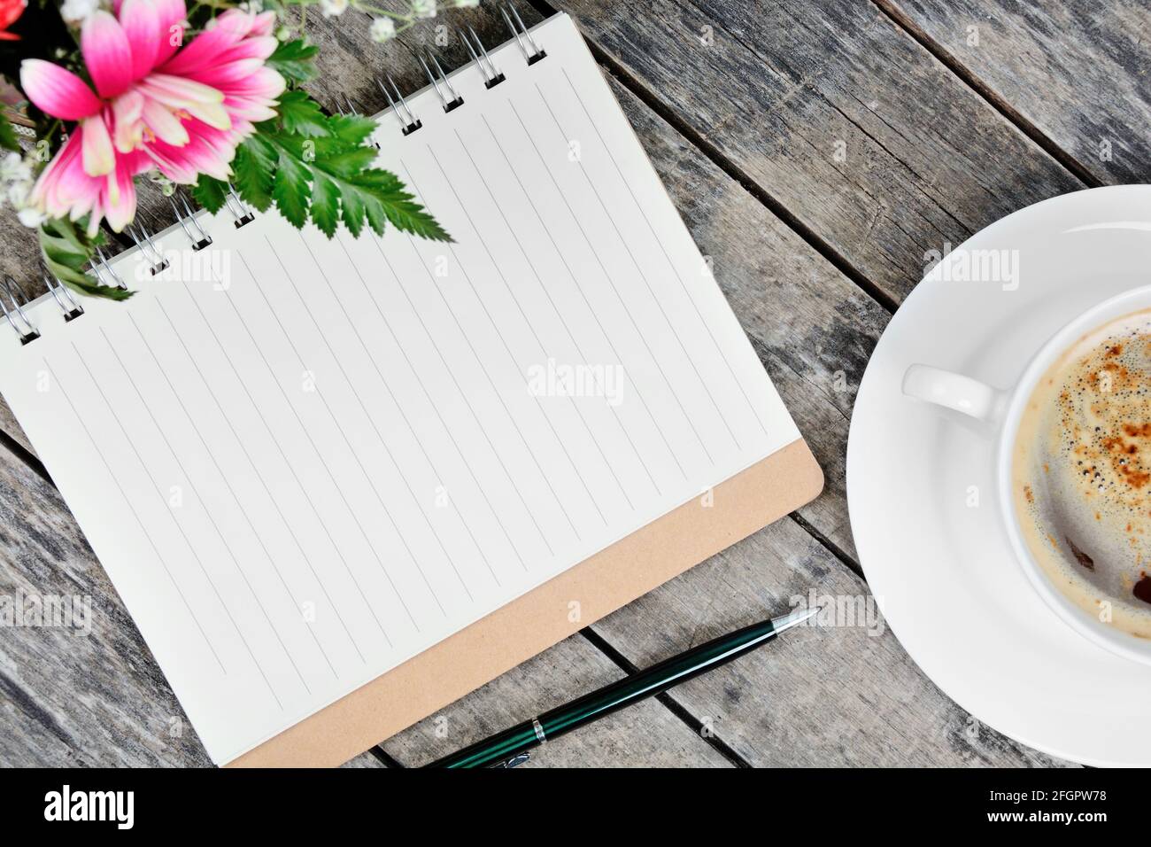 Close up of empty notebook with pen, coffee cup and flowers on table Stock Photo