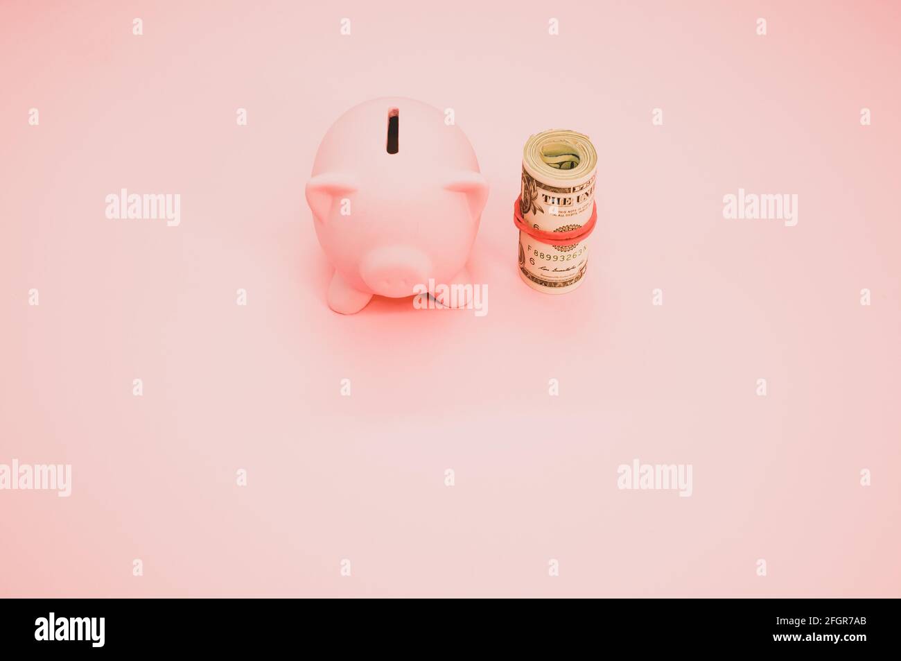 A top view of a piggy bank next to a roll of dollars isolated on pink ...