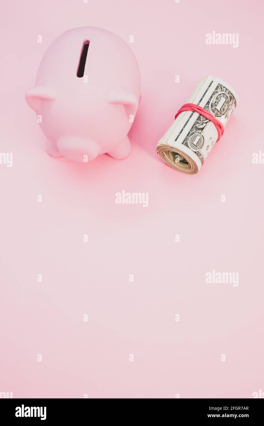 A top view of a piggy bank next to a roll of dollars isolated on pink ...