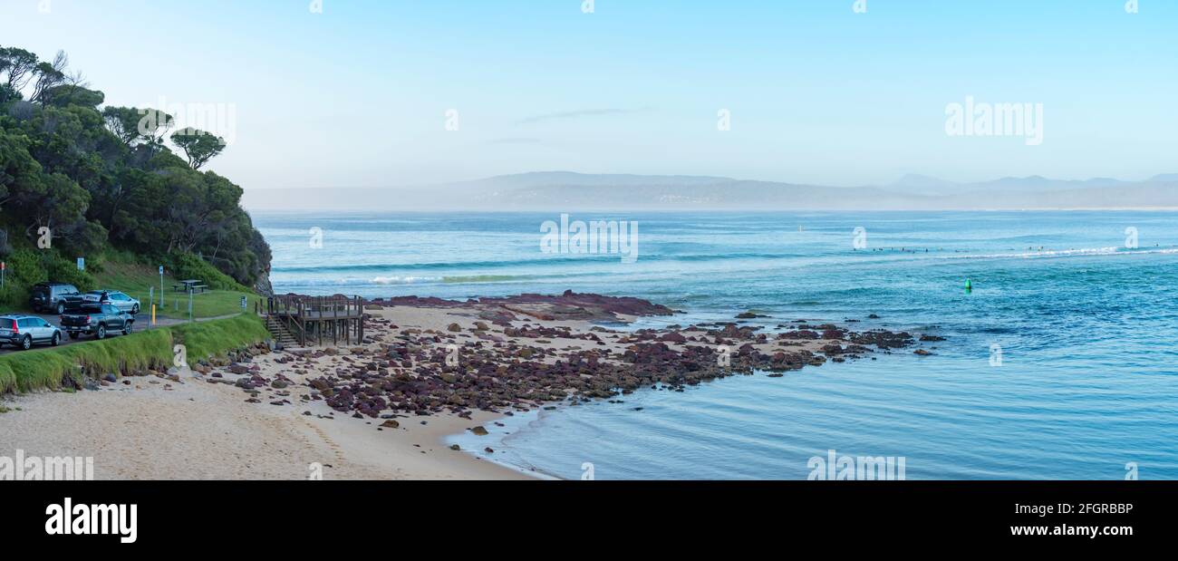 An early morning panorama of board riders waiting for the right wave at Bar Beach in Merimbula on the New South Wales south coast of Australia Stock Photo