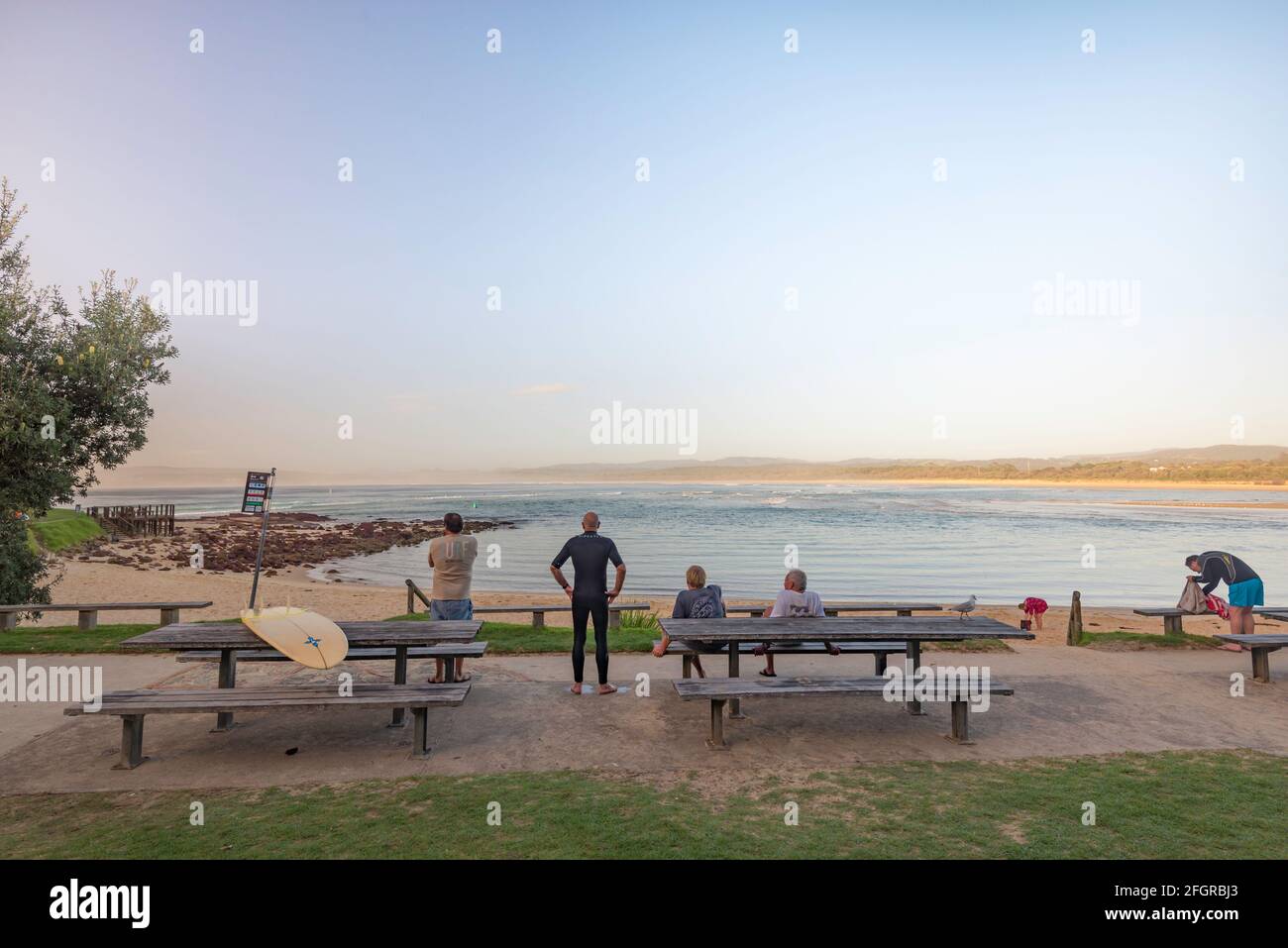 Boardriders young and old watch the surf at Bar Beach in Merimbula on the New South Wales south coast of Australia in the early morning Stock Photo