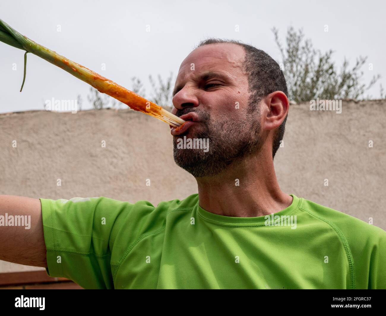 A Spanish male eating barbecue of spring onion shoots with tomato sauce
