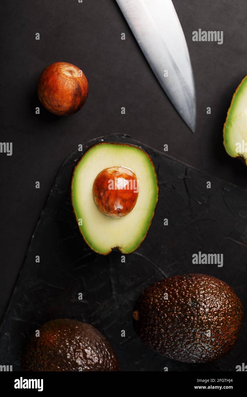 Sliced and whole organic avocado Hass with a knife on a black