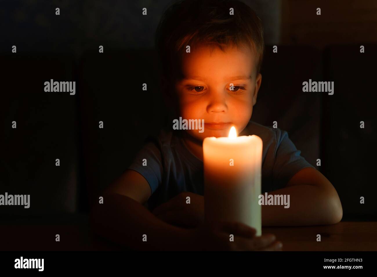 little kid boy of four years old admires a burning wax candle in the