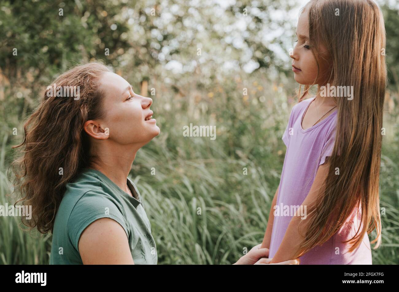 a mother with a small intra channel hearing aid communicates with her little daughter in nature outdoor Stock Photo