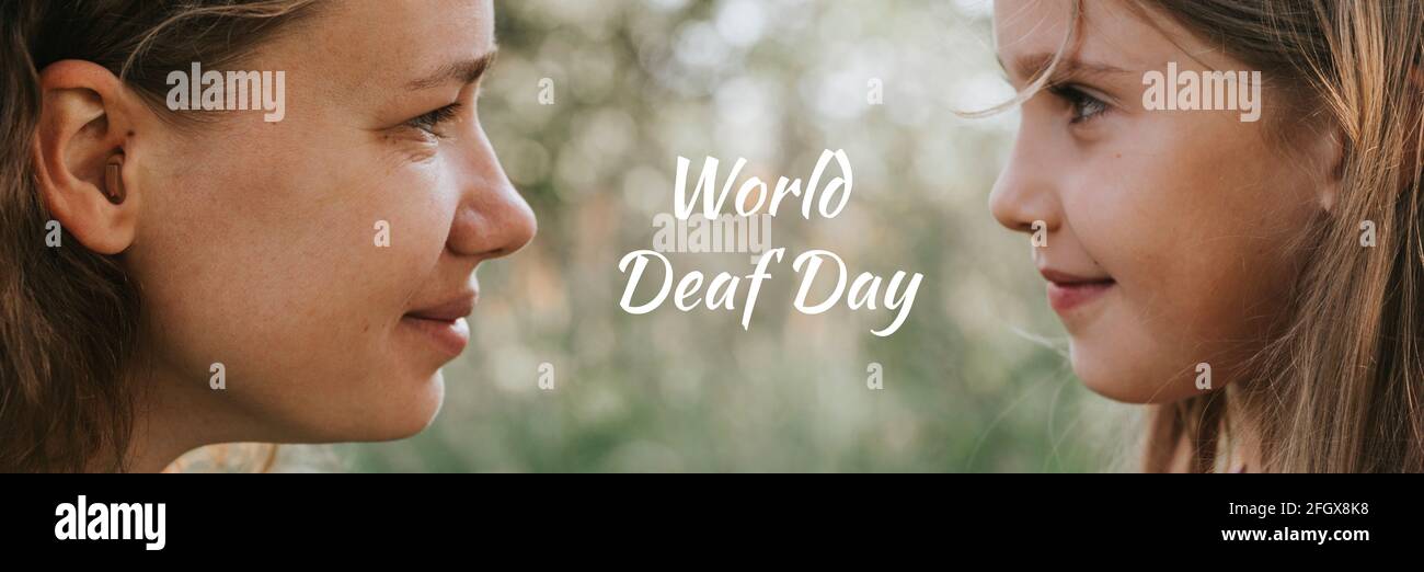 a mother with a small intra channel hearing aid communicates with her little daughter in nature outdoor. banner. text 'World Deaf Day' OFL font Stock Photo