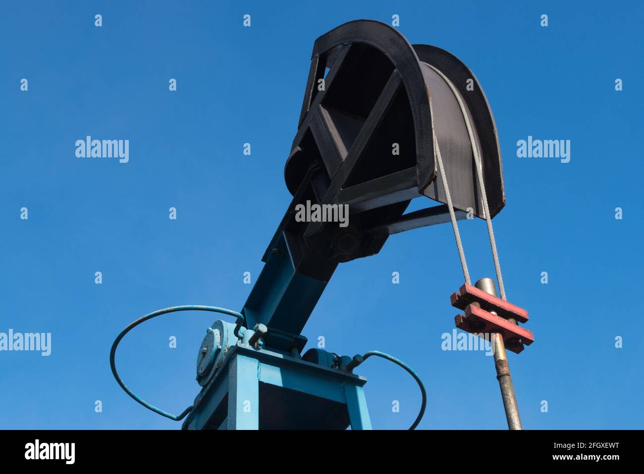 Industrial block pumping unit with blue painted installation frame and black sucker rod with flexible rope and red clamping element on the background Stock Photo