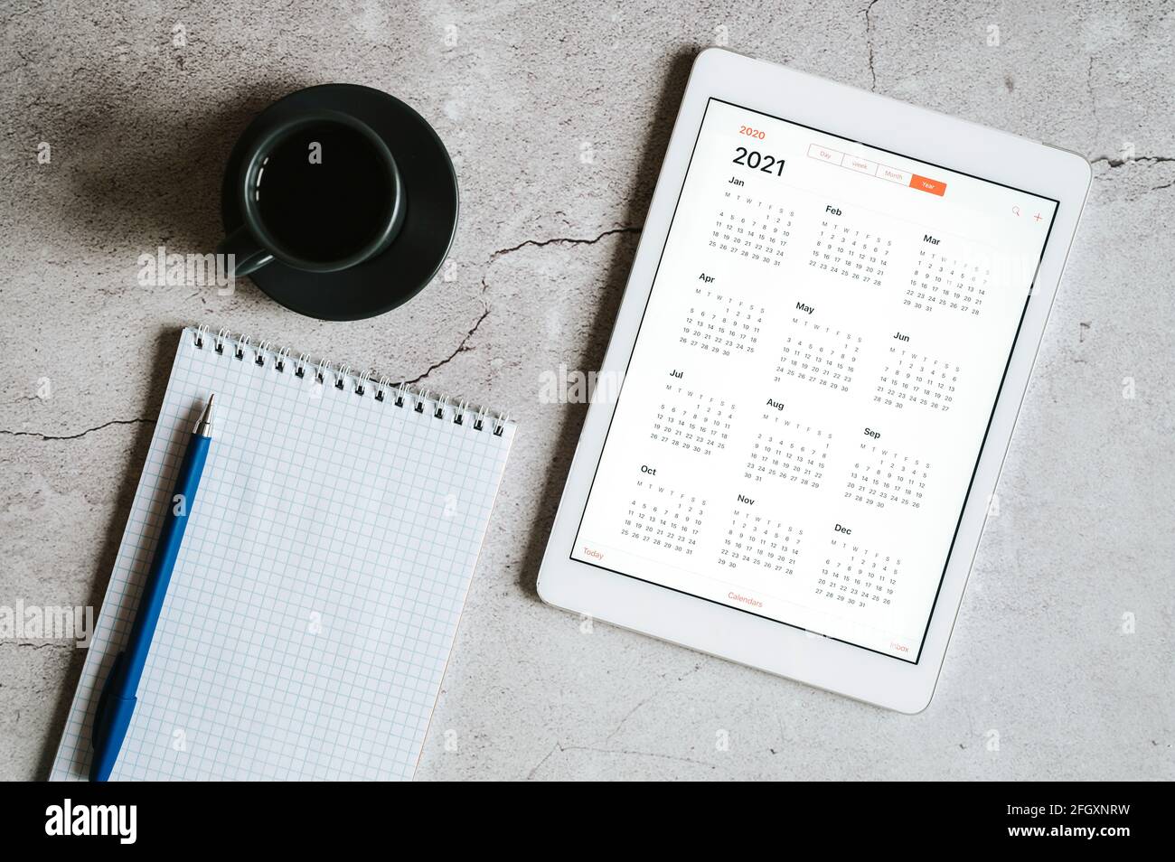 a tablet with an open calendar for 2021 year, a cup of coffee, and a ...