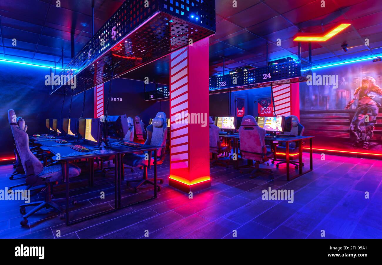 Torrevieja, Spain - April 15, 2021: Inside of empty internet cafe, glow neon illuminated cybercafe room with computers on tables, no people. Stock Photo