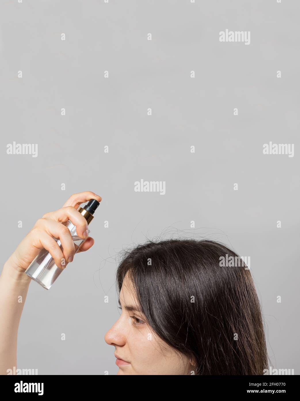 The girl puts on her hair a tonic of hydrolyte from a bottle. Hair care at home. Vertical photo with place for text. Stock Photo