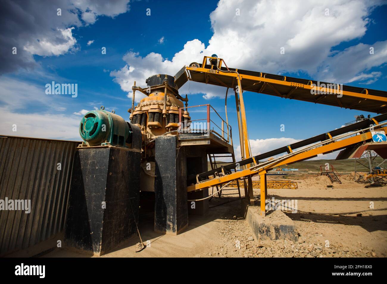 Rock crushing plant. Gravel separation machine. Construction materials production. Yellow conveyor belts and cone crusher. Green electric motor. Stock Photo
