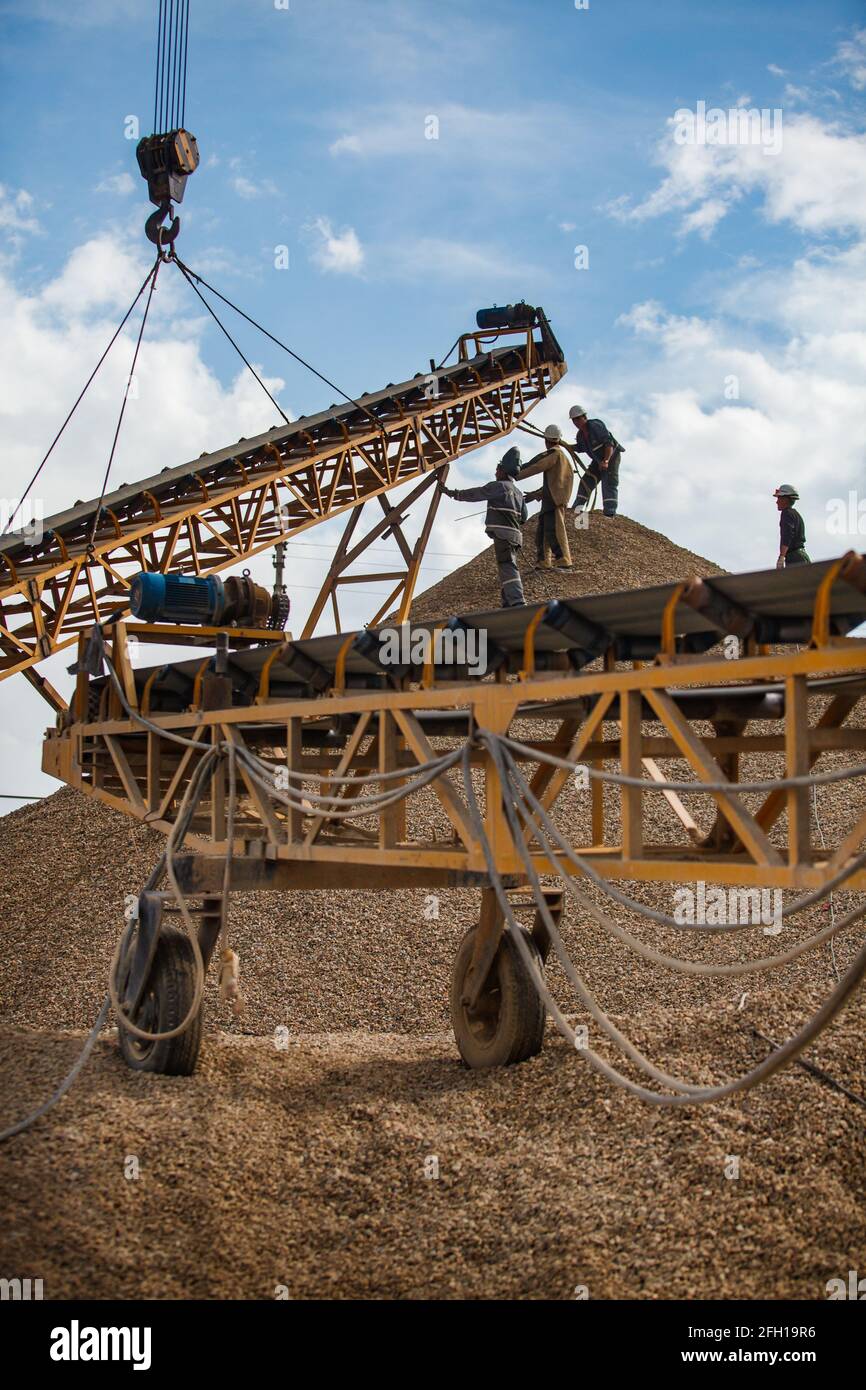 Mining and processing plant.Workers assembling rock crushing machine for gold ore shredding.Lifting by crane.Blue sky,clouds.Almaty region,Kazakstan. Stock Photo