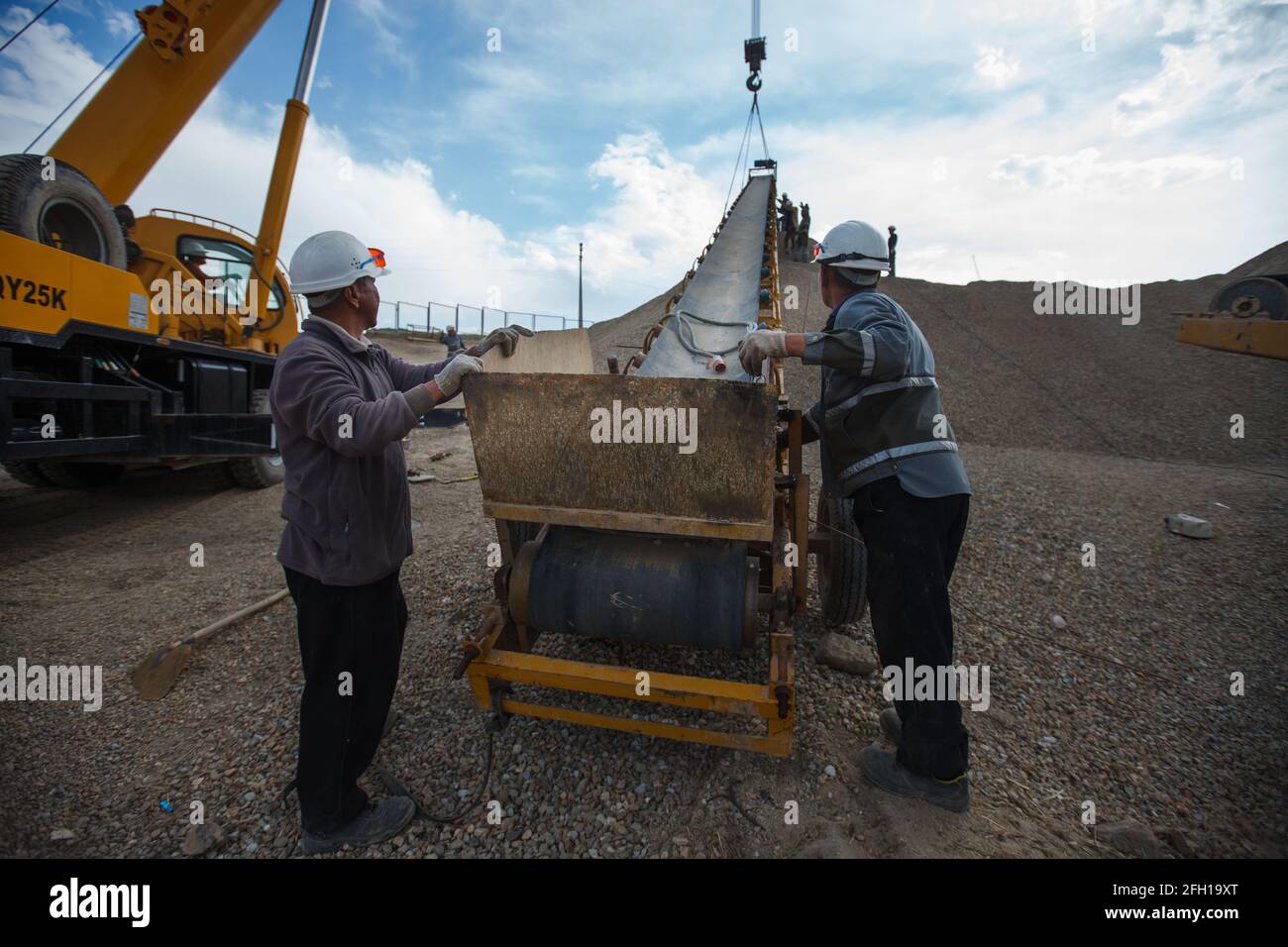 Mining and processing plant Altynalmas. Workers assembling rock crushing machine, using for gold ore shredding. Yellow mobile crane left. Stock Photo