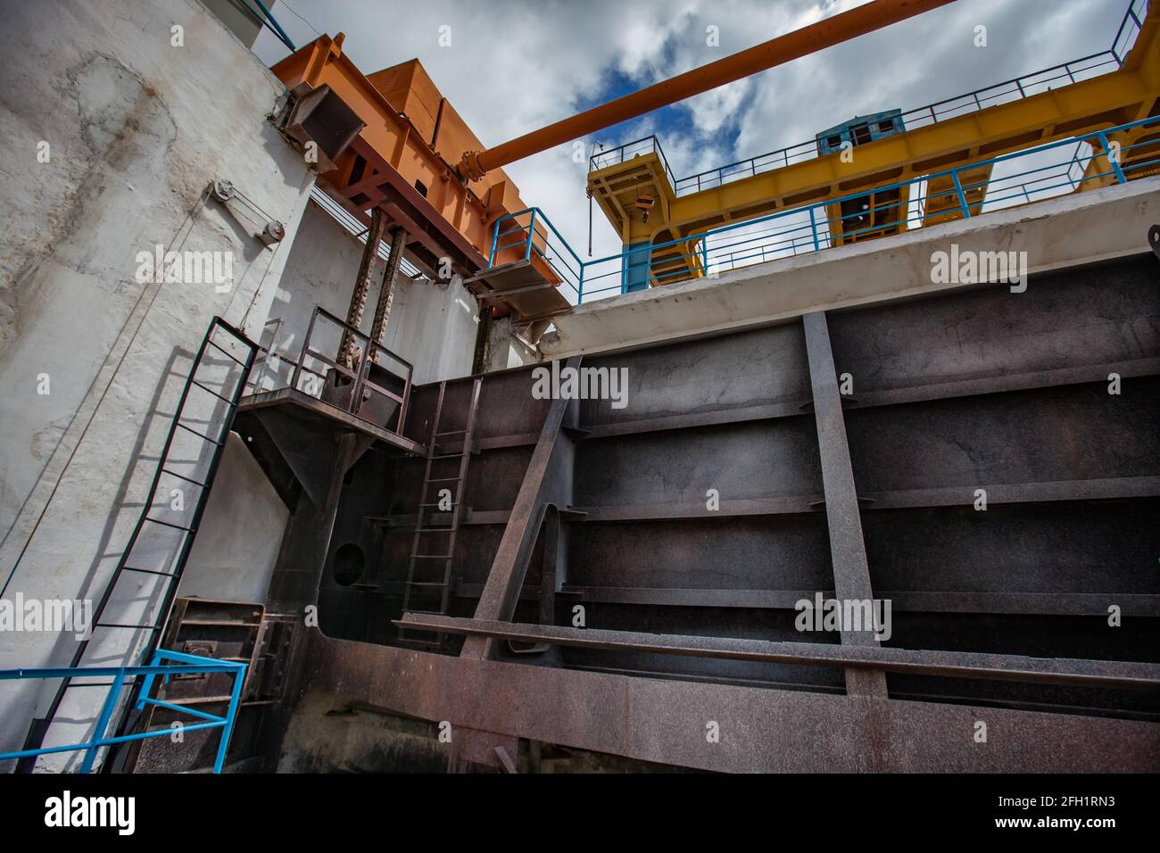 Lifting mechanism of water shutter. Shardara river dam. Grey metal shutter and yellow overhead crane. Kazaly city, Kyzylorda region, Kazakhstan. Stock Photo