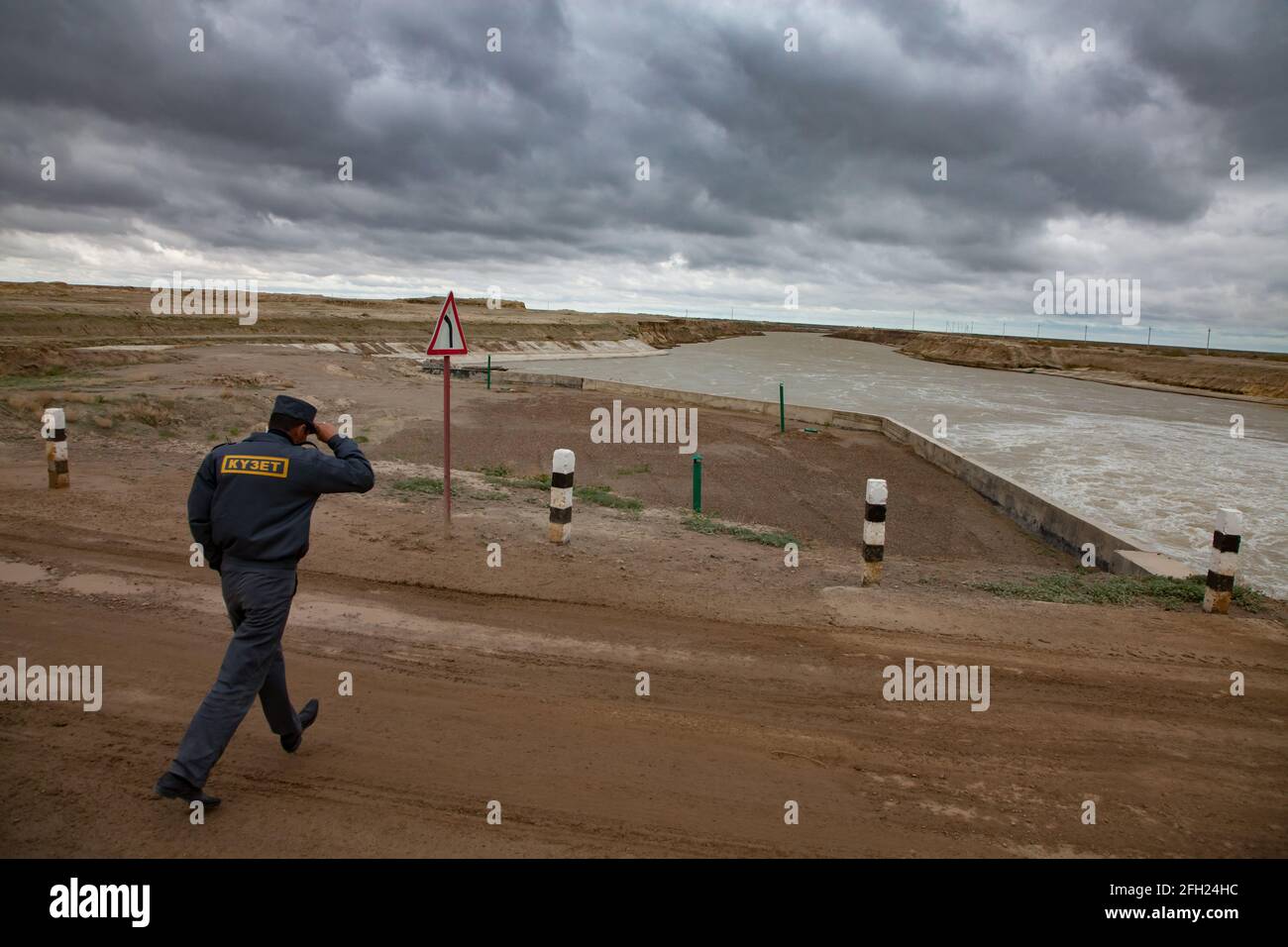 Kzylorda region,Kazakhstan:Aklak dam on Shardara river.Title:Security guard.Man run under strong wind.Turbulent water and storm clouds Stock Photo