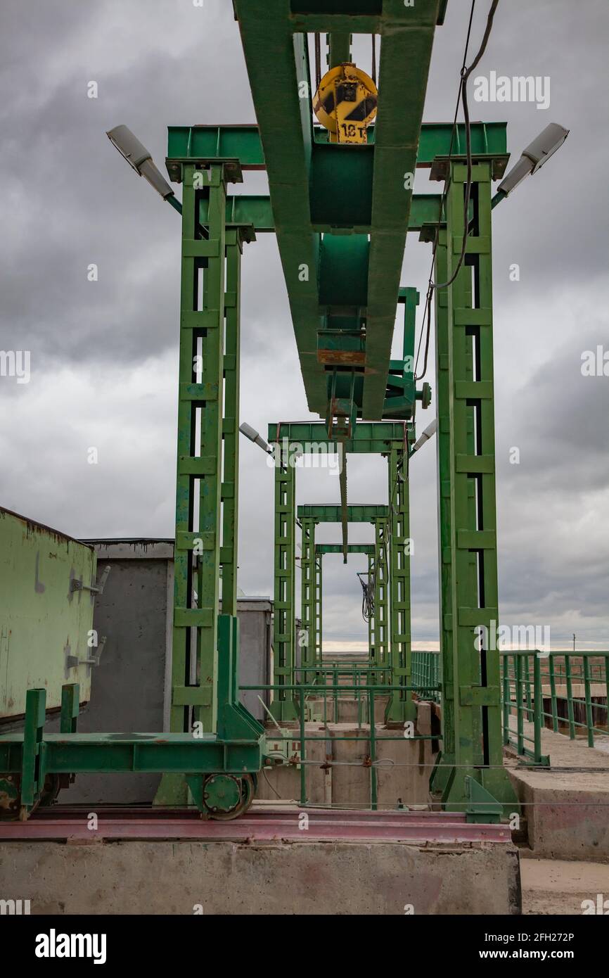 Aklak dam on Shardara river. Lifting device of water shutter metal  weights. Electric crane on rails. Grey storm sky. Kazakhstan, Kzylorda region. Stock Photo
