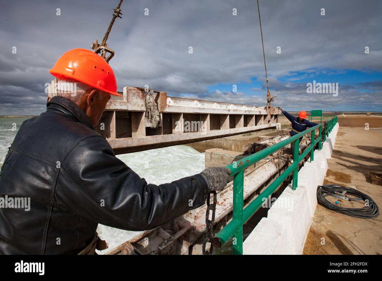 Kok-aral,Kazakhstan:Small Aral Sea Kok-aral dam.Two workers in orange helmets hoist water shutter weighting agent (steel girder) by crane. Stock Photo