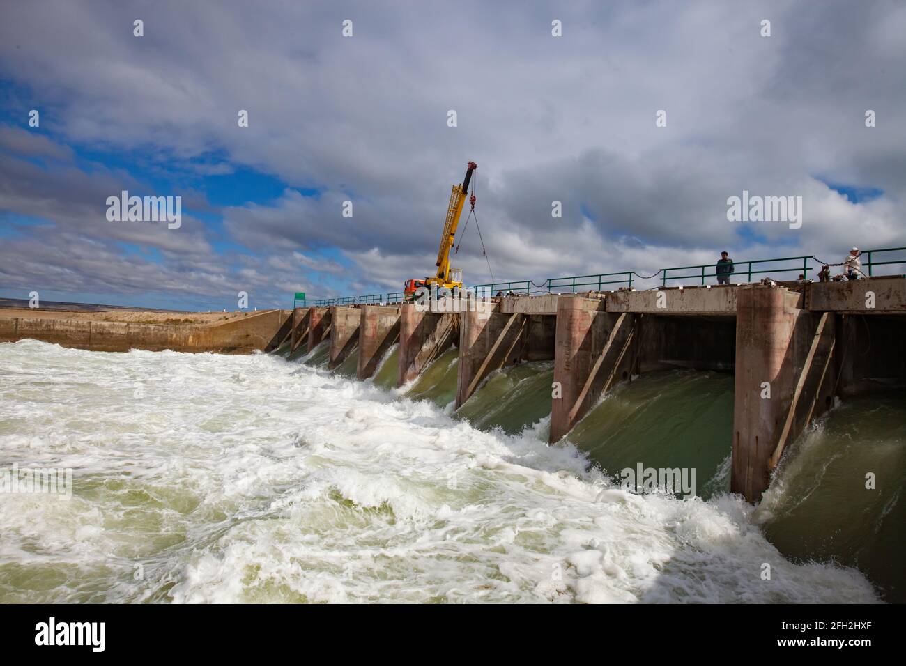 Kazakhstan, small Aral sea Kok-aral dam. Water discharge in flood. Open shutters. Yellow mobile crane and workers on dam. Stock Photo