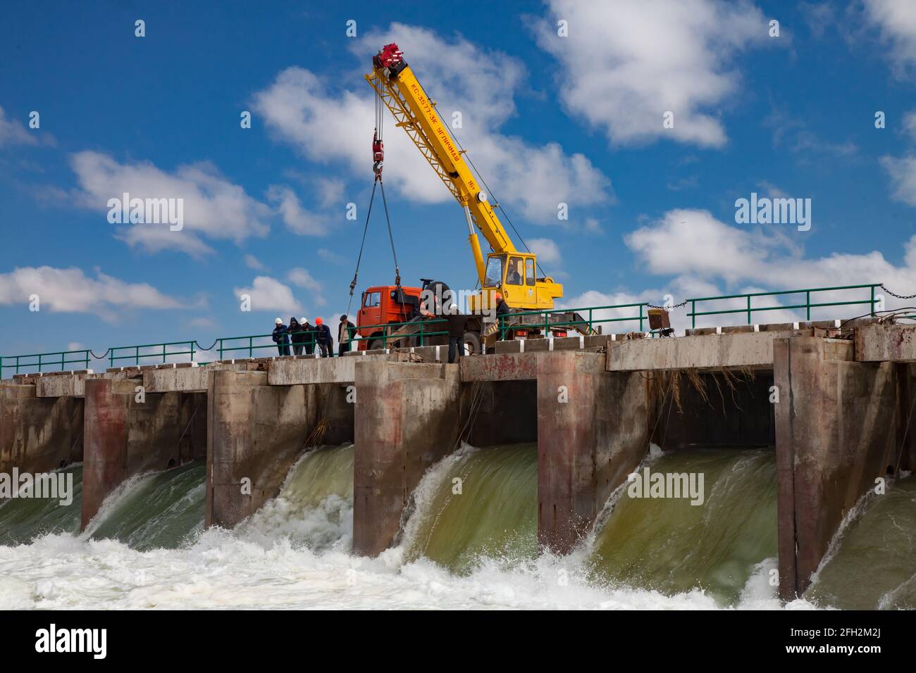 Kok-aral,Kazakhstan: Aral Sea Kok-aral dam. Water discharge in flood. Open shutters. Yellow mobile crane and workers on dam. Stock Photo