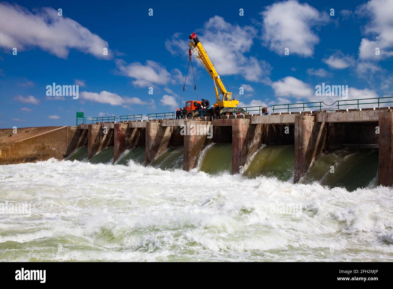 Kok-aral, Kazakhstan: Aral Sea Kok-aral dam. Water discharge in flood.Open shutters.Yellow mobile crane and workers on dam. Stock Photo