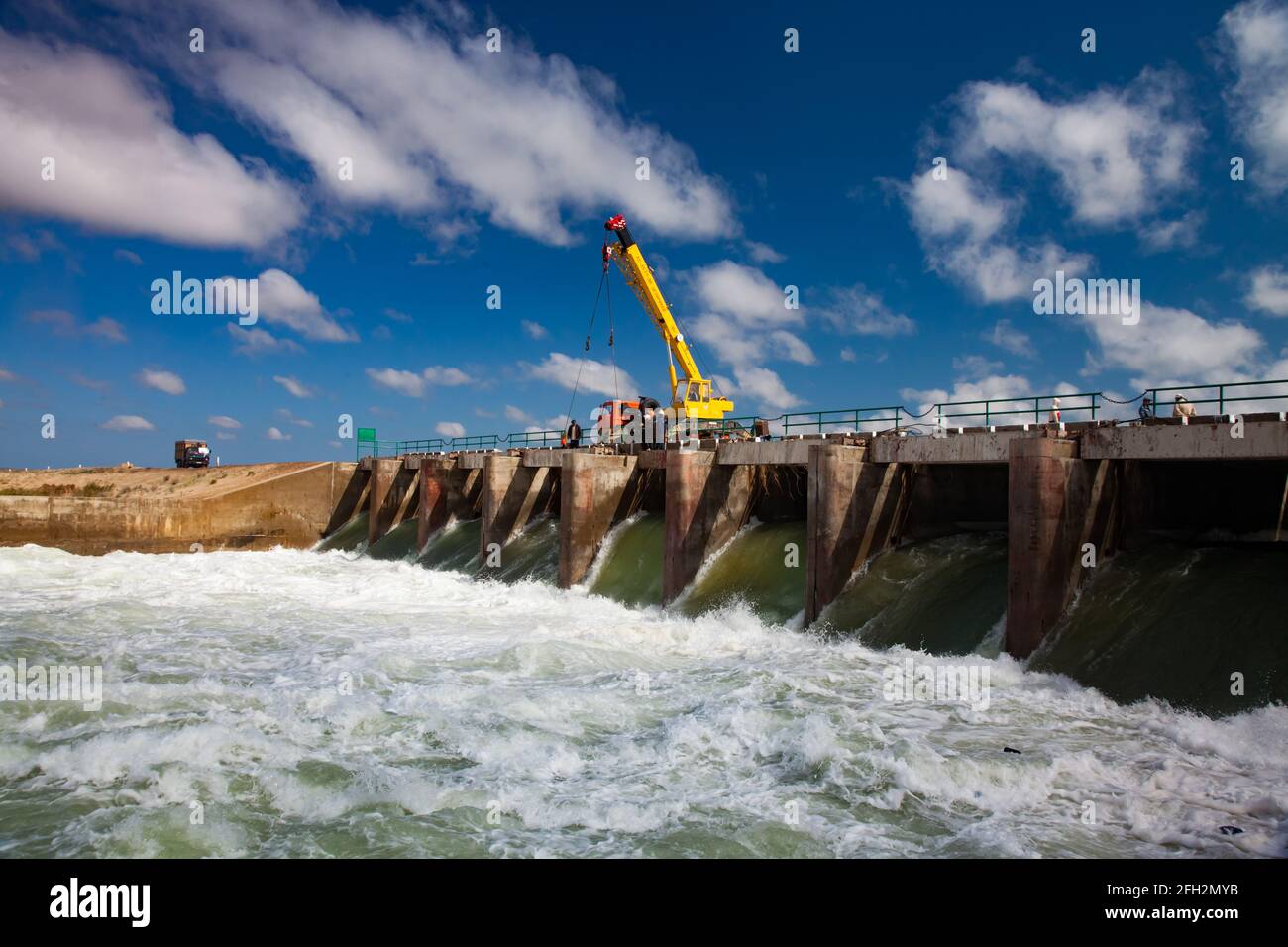 Kok-aral,Kazakhstan:Aral Sea Kok-aral dam.Water discharge in flood.Open shutters.Yellow mobile crane and workers on dam Stock Photo