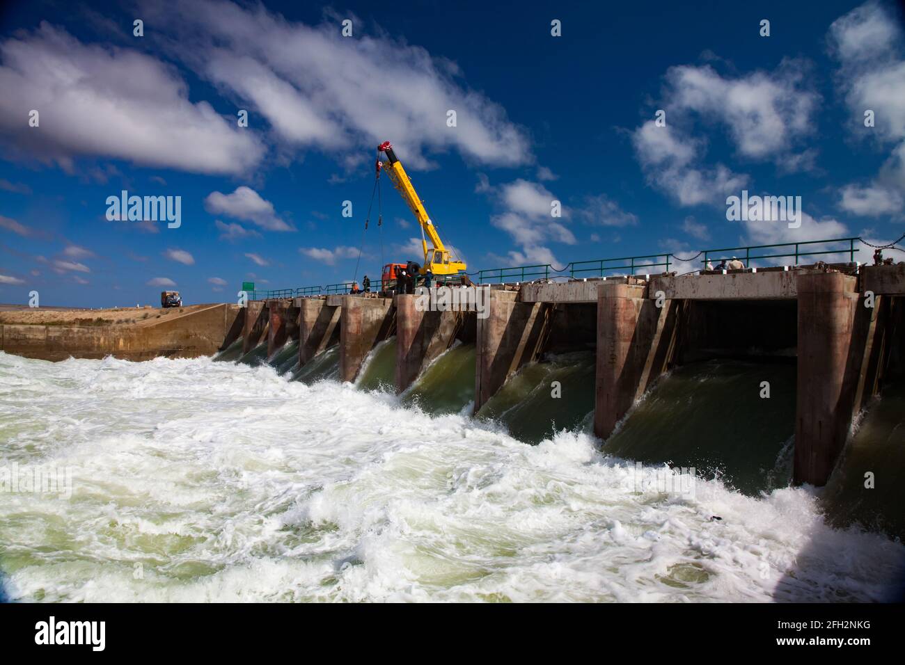 Kok-aral,Kazakhstan:Aral Sea Kok-aral dam. Water discharge in flood.Open shutters. Yellow mobile crane and workers on dam. Stock Photo
