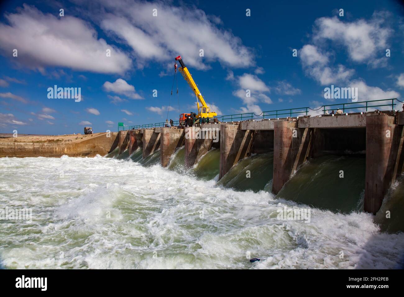 Kok-aral,Kazakhstan: Aral Sea Kok-aral dam.Water discharge in flood.Open shutters.Yellow mobile crane and workers on dam. Stock Photo
