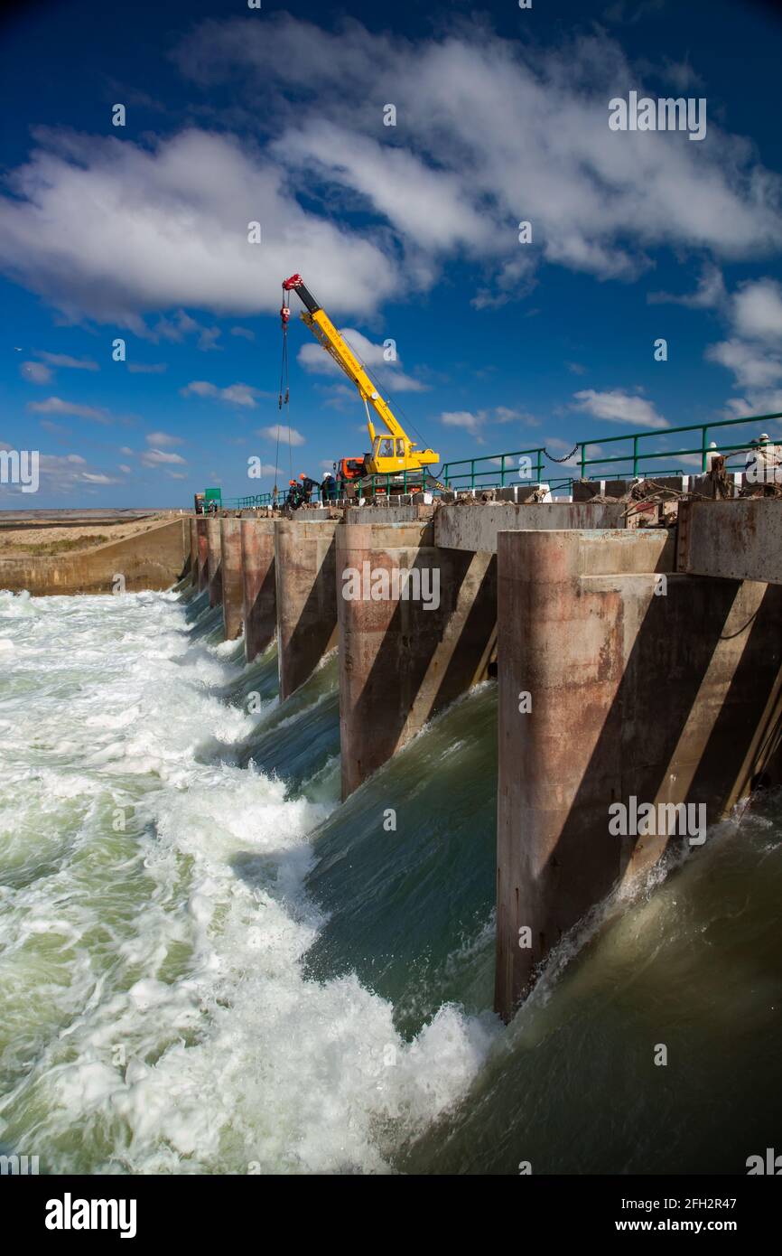Kazakhstan, Small Aral Sea Kok-aral dam. Water discharge in flood. Open shutters. Yellow mobile crane and workers on dam. Stock Photo