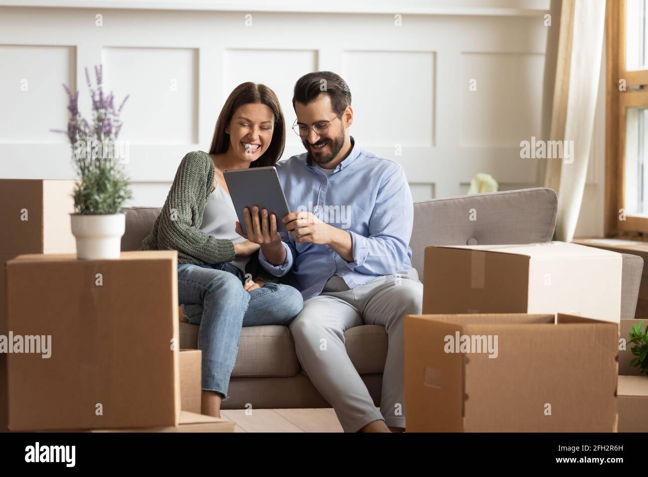 Happy couple relax on sofa using tablet on relocation day Stock Photo