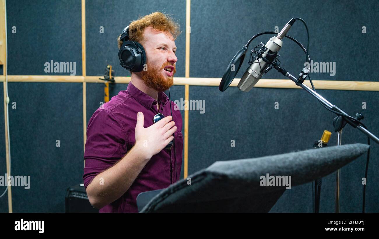 Expressive bearded man with curly ginger hair in headphones at recording studio Stock Photo