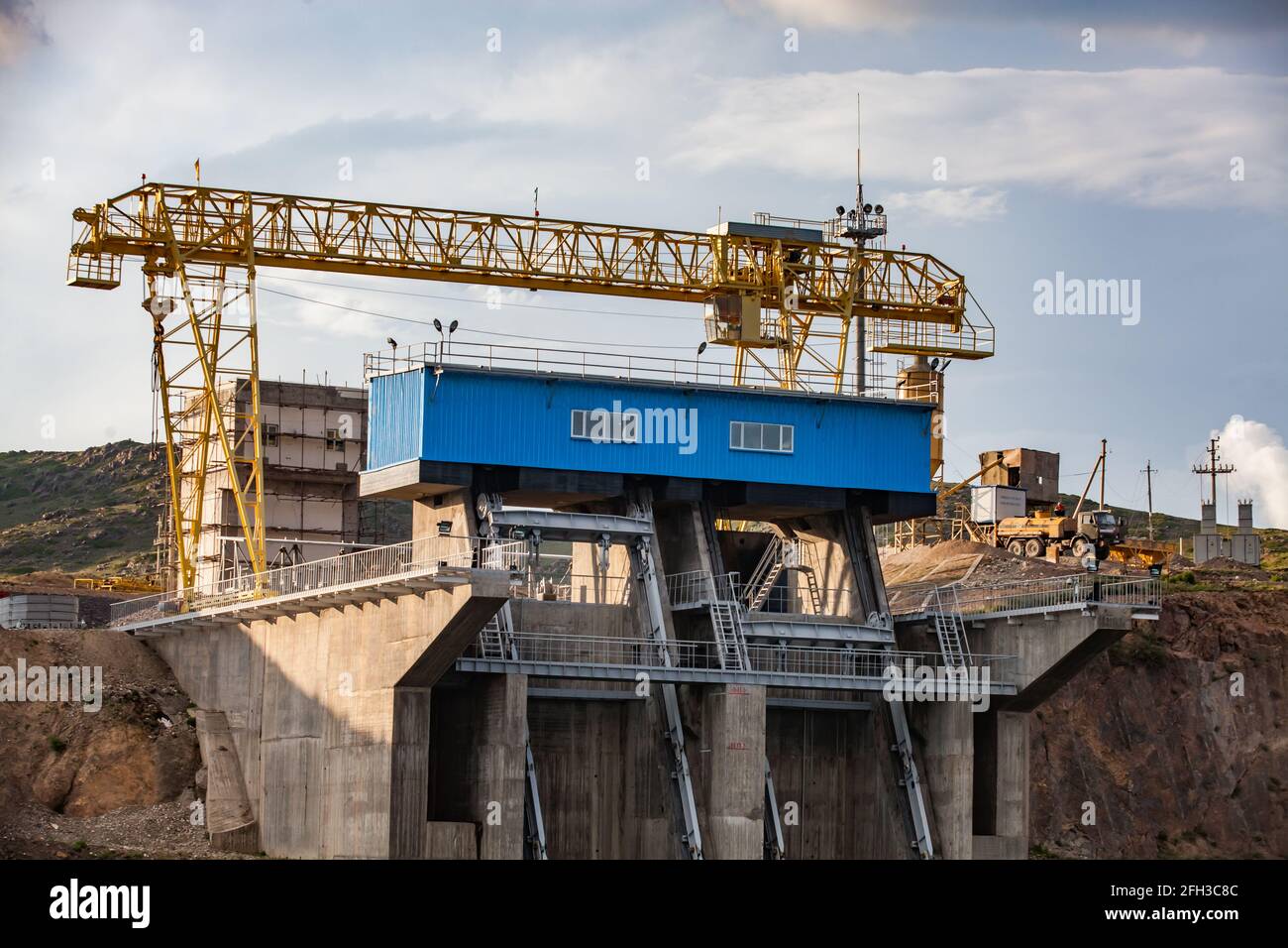Dam on Sharyn river. Close up photo. Blue machine house, yellow gantry crane. Blue sky with clouds background. Almaty region, Kazakhstan. Stock Photo