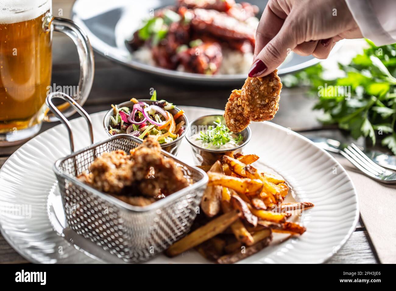 Crispy breaded chicken nuggets with french fries served on a plate with a dip and a salad. Stock Photo