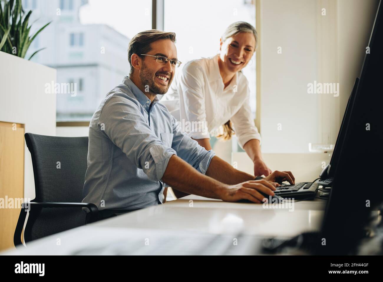 business partners working together on computer. Colleagues smiling and discussing project on computer. Stock Photo