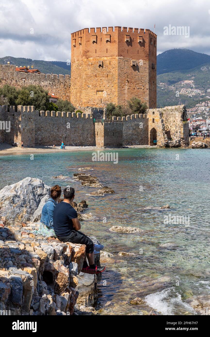 Couple watching the historical Kizil Kule, Red Tower, in Alanya Castle during the coronavirus pandemic days in Alanya, Antalya, Turkey. Stock Photo