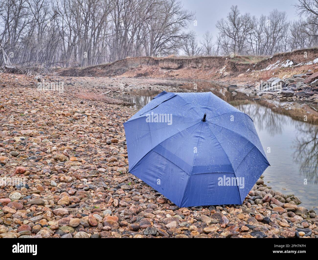 umbrella on a river shore in early spring scenery with a low water and falling snow Stock Photo