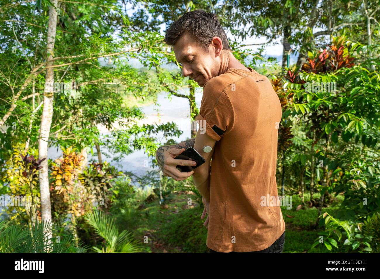 Young Man with Diabetic type 1 is measuring his blood sugar level with Abbott Freestyle Libre 2 sensor on the arm as he travels outdoor.Amazon rainfor Stock Photo